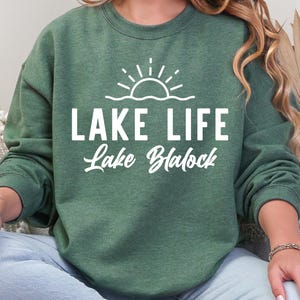 May include: Dark green sweatshirt with the words "LAKE LIFE Lake Blalock" in white script and a sun and wave graphic. The sweatshirt is a heathered dark green color.