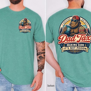 Puede incluir: Camiseta verde mar con un gr&aacute;fico de Bigfoot. El gr&aacute;fico frontal dice "Dad Tax" y "Making Sure It's Not Poison". El gr&aacute;fico trasero presenta a Bigfoot con gafas de sol y gorra roja, sosteniendo una bebida y papas fritas. El texto dice "Certified Dad Duty".