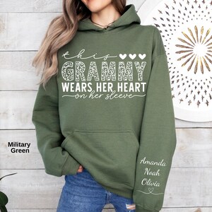 May include: Military green hoodie with the text "this Grammy wears her heart on her sleeve." The word "Grammy" has a leopard print design. The names Amanda, Noah, and Olivia are printed on the sleeve.