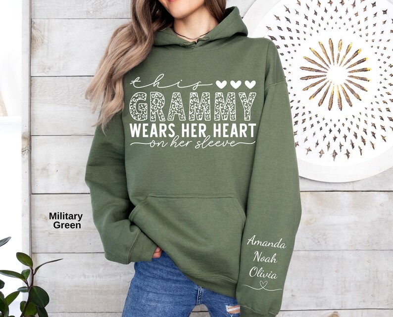 May include: Military green hoodie with the text "this Grammy wears her heart on her sleeve." The word "Grammy" has a leopard print design. The names Amanda, Noah, and Olivia are printed on the sleeve.
