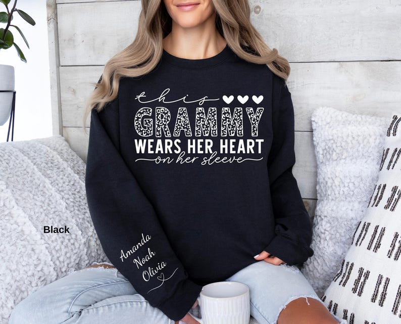 May include: Black sweatshirt with the text "this Grammy wears her heart on her sleeve." The word "Grammy" is in a leopard print design. The names "Amanda, Noah, Olivia" are printed on the left sleeve. The sweatshirt is a crew neck.