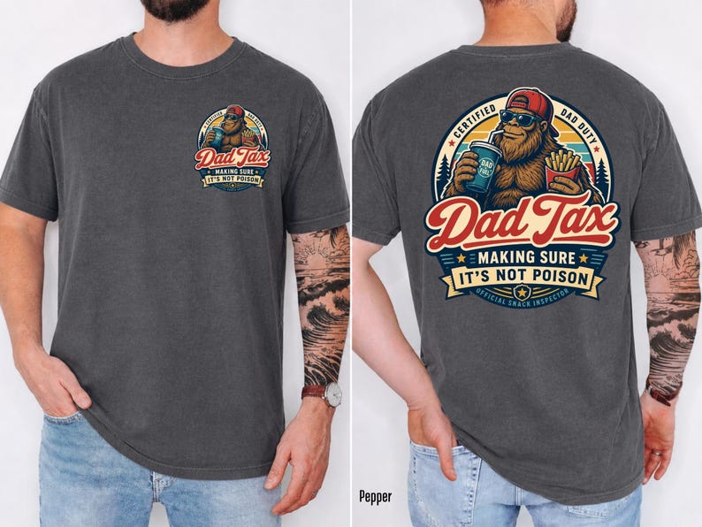 May include: Dark grey t-shirt with a Bigfoot graphic on the front and back. The front graphic says "Dad Tax" with a Bigfoot illustration. The back graphic says "Dad Tax" with a Bigfoot holding a drink and fries. The text on the back says "Making sure it's not poison."