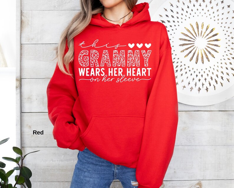 May include: A red hooded sweatshirt with the text "this Grammy wears her heart on her sleeve" in white script and a leopard print design. The sweatshirt has a front pocket and a drawstring hood.