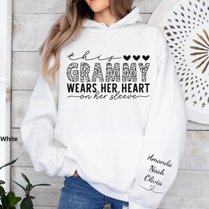May include: White hoodie with the text "this Grammy wears her heart on her sleeve" in black script and leopard print. The sleeve features the names Amanda, Noah, and Olivia in black script. The hoodie has a front pocket and a hood.