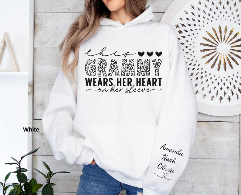 May include: White hoodie with the text "this Grammy wears her heart on her sleeve" in black script and leopard print. The sleeve features the names Amanda, Noah, and Olivia in black script. The hoodie has a front pocket and a hood.