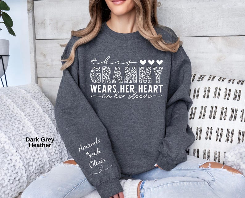 May include: Dark gray heather sweatshirt with the text "this grammy wears her heart on her sleeve" in white. The word "grammy" is in a leopard print pattern. The names Amanda, Noah, and Olivia are printed on the sleeve.