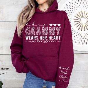 May include: Maroon hoodie with the text "this Grammy wears her heart on her sleeve" in white script. The word "Grammy" has a leopard print design. The sleeve has the names Amanda, Noah, and Olivia in white script.
