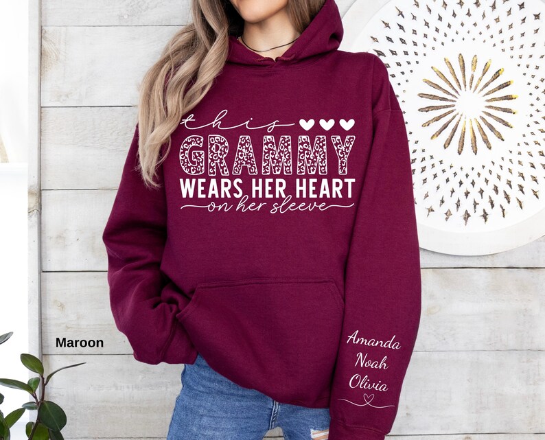 May include: Maroon hoodie with the text "this Grammy wears her heart on her sleeve" in white script. The word "Grammy" has a leopard print design. The sleeve has the names Amanda, Noah, and Olivia in white script.
