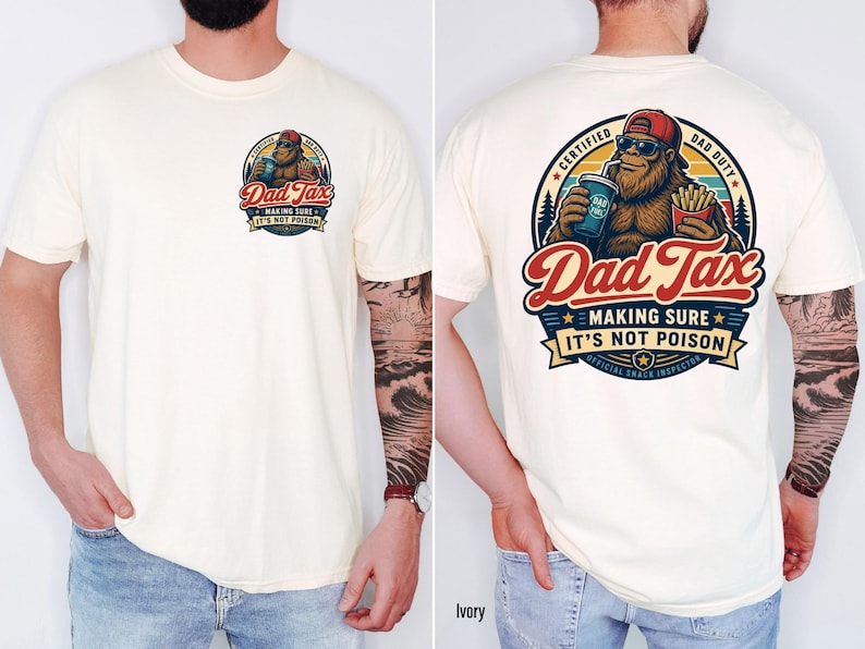 Puede incluir: Camiseta de color crema con un gr&aacute;fico en la parte delantera y trasera. El gr&aacute;fico de la parte delantera muestra el texto "Dad Tax" y un dibujo de Bigfoot. El gr&aacute;fico de la parte trasera es una versi&oacute;n m&aacute;s grande del mismo dise&ntilde;o, con texto adicional.