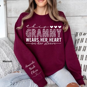 May include: Maroon sweatshirt with the text "this Grammy wears her heart on her sleeve" in white script and leopard print. The sleeve has the names "Amanda, Noah, Olivia" in white script. The sweatshirt is a solid maroon color.