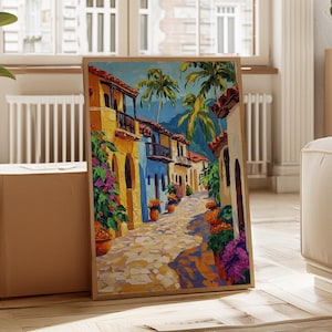 May include: A framed painting of a colourful street scene, featuring buildings in yellow and blue. Palm trees and flowers adorn the cobblestone street, set against a bright blue sky. The artwork is presented in a light-coloured wooden frame.