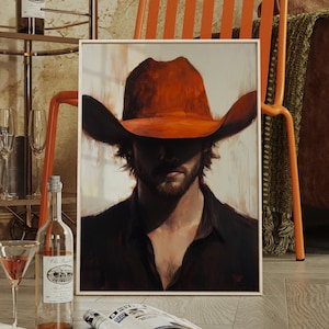May include: A framed painting of a man wearing a large orange cowboy hat. The man is looking down with a serious expression. The painting is hanging on a wall in a room with a wooden floor and a leather couch.
