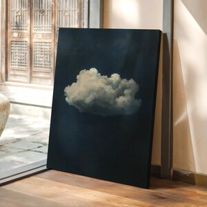 May include: A canvas art print featuring a fluffy white cloud against a dark blue background. The artwork is leaning against a wall in a room with wooden floors and a view of an outdoor courtyard through a large window.