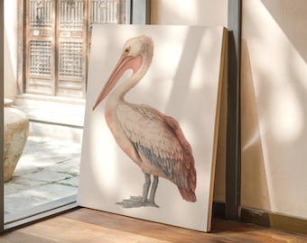 Op de afbeelding: Een aquarel schilderij van een pelikaan in roze, beige en grijstinten. De vogel staat afgebeeld op een wit canvas, leunend tegen een muur. Het kunstwerk wordt binnenshuis tentoongesteld, in de buurt van een raam met uitzicht op een binnenplaats.
