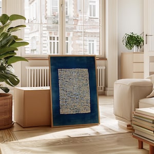 May include: A framed abstract art print featuring a dark blue background with a pattern of small, evenly spaced white dots. The artwork is displayed in a light brown wooden frame, adding a touch of warmth to the piece. The print is placed in a well-lit room with a large window.