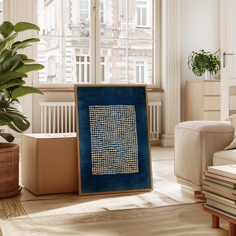 May include: A framed abstract art print featuring a dark blue background with a pattern of small, evenly spaced white dots. The artwork is displayed in a light brown wooden frame, adding a touch of warmth to the piece. The print is placed in a well-lit room with a large window.