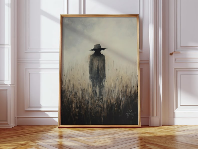 Peut inclure: Une &oelig;uvre d'art encadr&eacute;e repr&eacute;sente une silhouette portant un chapeau dans un champ d'herbes hautes. L'&oelig;uvre est r&eacute;alis&eacute;e dans des tons sourds de gris, de brun et de beige, avec une qualit&eacute; douce et atmosph&eacute;rique. Le cadre est de couleur bois clair.