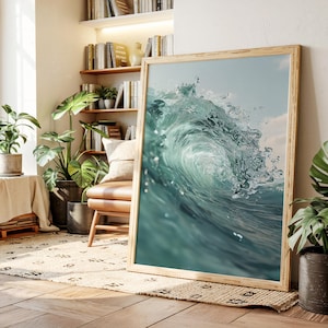 Puede incluir: Una impresión enmarcada que presenta un primer plano de una ola rompiendo en el océano. La imagen captura el agua turquesa arremolinada y la cresta de la ola, con un cielo azul claro en el fondo. El marco de madera añade un toque natural.