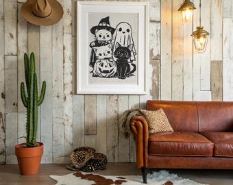 May include: A framed black and white Halloween-themed print featuring cartoon cats, a ghost, and a jack-o'-lantern. A brown hat hangs on the wall above a cactus in a terracotta pot. A brown leather sofa and a cowhide rug complete the scene.