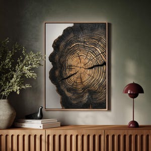 May include: A framed print of a tree trunk cross-section, showing the rings and texture of the wood. The wood is dark brown and black, with a light brown center. The print is hanging on a wall above a wooden cabinet.