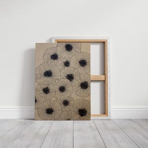 May include: A canvas art print featuring a cluster of stylized black and white flowers. The artwork is mounted on a white wooden frame, with the back of the canvas visible. The flowers have a detailed, radial design.