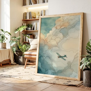 May include: A framed art print featuring a watercolor painting of a biplane flying through a cloudy sky. The artwork has a light wooden frame and a color palette of blues, beige, and peach.