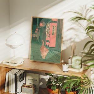 May include: A framed art print depicting a street scene in Japan with a cat. The artwork features a pink vending machine, red lanterns, and a cat with orange and brown stripes. The color palette includes shades of green, pink, and orange.