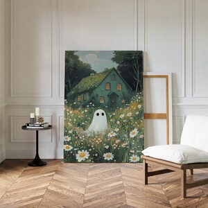May include: An art print depicting a teal house in a field of daisies, with a ghost. The artwork has a soft, dreamy quality, ideal for adding a touch of fantasy to any room. The print is displayed in a room with a wooden floor.