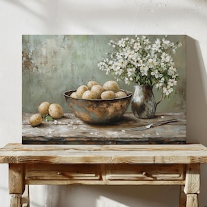May include: A still-life painting shows a bowl of potatoes, a vase of white flowers, and a fork on a wooden table. The bowl has a weathered, metallic look. The background is a muted green. The scene evokes a rustic feel.