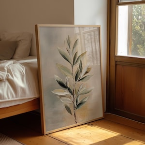May include: A framed botanical print depicting a detailed illustration of a leafy branch. The artwork uses a muted palette of greens, creams, and browns, with a light wooden frame. The painting is leaning against a wall near a window.