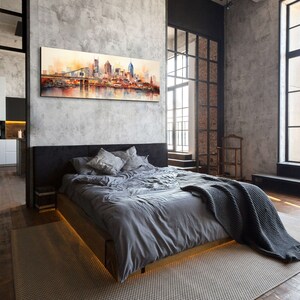 Op de afbeelding: Een moderne slaapkamer met een grijs bed, een grijs deken en een groot schilderij van een skyline boven het bed. De kamer heeft grote ramen met zwarte kozijnen en een betonnen muur.