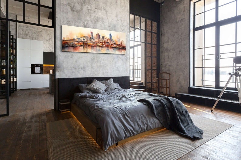 Op de afbeelding: Een moderne slaapkamer met een grijs bed, een grijs deken en een groot schilderij van een skyline boven het bed. De kamer heeft grote ramen met zwarte kozijnen en een betonnen muur.