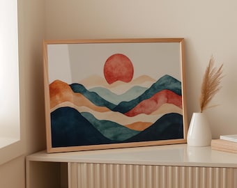 Può includere: Una stampa ad acquerello incorniciata raffigurante un paesaggio montano stilizzato con un grande sole rosso. Le montagne sono raffigurate in tonalità di blu, arancione e rosso. La cornice è in legno chiaro. Un vaso bianco con piante secche è su una superficie vicina.