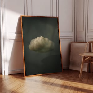 May include: A framed art print featuring a fluffy white cloud against a dark gray background. The artwork is displayed in a room with wooden floors and white paneling. The frame is a warm brown color.