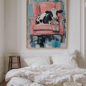 Puede incluir: Una vaca negra y blanca sentada en un sill&oacute;n rosa. El sill&oacute;n est&aacute; frente a una pintura abstracta azul y blanca.