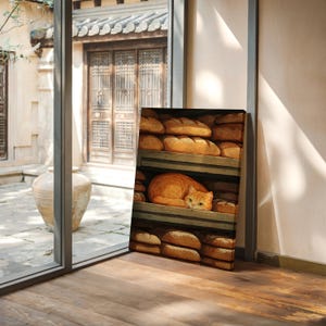 May include: A canvas print depicts a cozy scene of a ginger cat nestled among loaves of bread on wooden shelves. The artwork is set in a sunlit room, with a glimpse of an outdoor courtyard visible through a window.