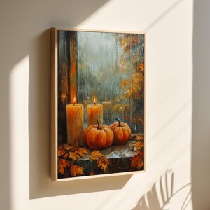 Puede incluir: Una pintura de una ventana con tres velas encendidas y dos calabazas en un alféizar. La ventana está abierta y está lloviendo afuera. La pintura está enmarcada en madera.