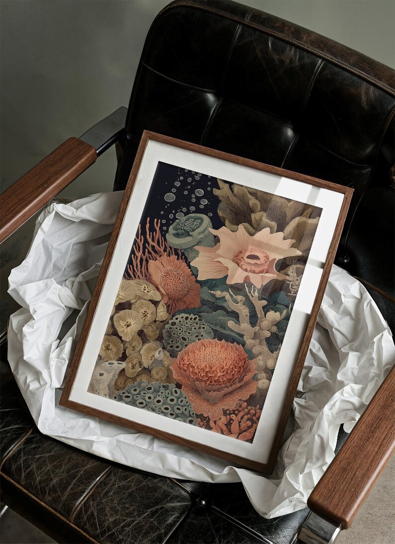 May include: A framed art print featuring a detailed illustration of a coral reef. The artwork showcases various coral formations in shades of orange, green, and beige against a dark blue background. The print is encased in a wooden frame and rests on white paper.