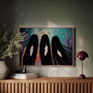 May include: A framed art print featuring three figures with long black hair, each adorned with a white feather. The artwork has a colorful background with butterflies and floral elements, set against a teal and purple backdrop.