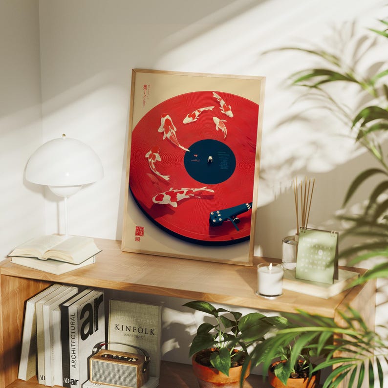 Puede incluir: Impresi&oacute;n art&iacute;stica enmarcada que presenta un dise&ntilde;o de disco de vinilo rojo con ilustraciones de peces koi. La obra de arte incluye un brazo de tono azul y una etiqueta central negra. La impresi&oacute;n se exhibe en una estanter&iacute;a de madera con libros y una l&aacute;mpara.