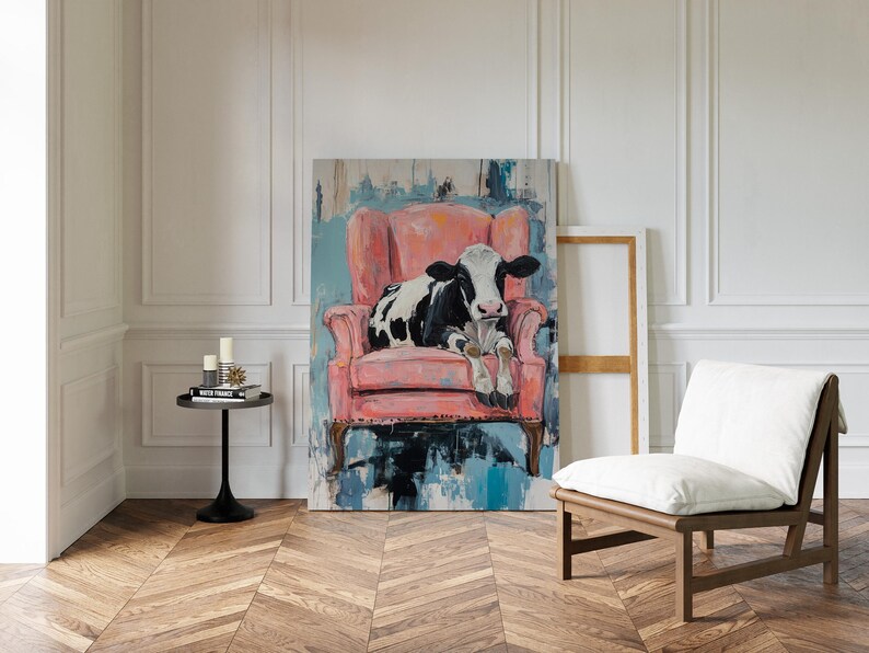 Puede incluir: Una vaca negra y blanca tumbada en un sill&oacute;n rosa. El sill&oacute;n est&aacute; delante de una pintura con pinceladas abstractas azules y blancas. La vaca mira al espectador.