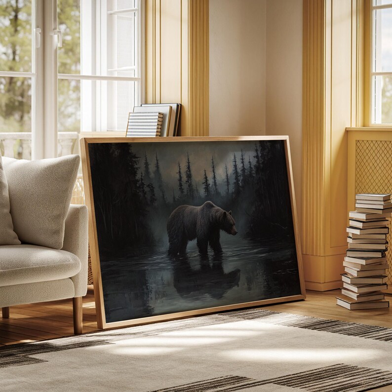 Op de afbeelding: Een ingelijst kunstwerk toont een bruine beer die door een donker, reflecterend water loopt, met een bos op de achtergrond. Het schilderij heeft een natuurlijke houten lijst en leunt tegen een muur. De sc&egrave;ne roept een gevoel van wildernis en rust op.