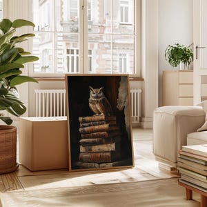 Op de afbeelding: Een ingelijste print met een gedetailleerd schilderij van een bruine uil die bovenop een stapel oude boeken zit. Het kunstwerk heeft een donkere, vintage esthetiek, met de veren van de uil en de pagina's van de boeken in detail weergegeven. De lijst is lichtbruin.