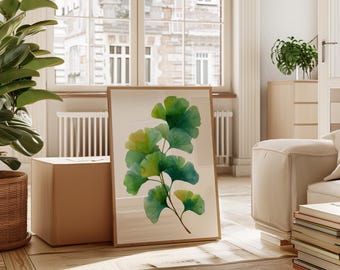May include: A framed art print featuring a watercolor illustration of ginkgo leaves in shades of green and yellow. The artwork is displayed in a light-colored wooden frame, leaning against a wall in a well-lit room with a window.