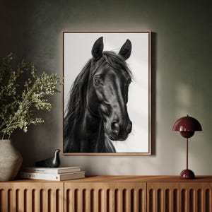 May include: A framed black and white portrait of a horse's head. The horse has a dark coat and long, flowing mane. The artwork is displayed on a wooden cabinet, with a vase of greenery and a red lamp.