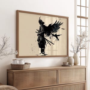 May include: Framed art print featuring a black ink illustration of a samurai warrior with a bird-like wing and two swords. The artwork is set against a beige background within a wooden frame. The print is displayed on a wooden cabinet.