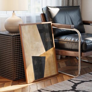 Può includere: Stampa artistica astratta con cornice in legno. L'opera presenta forme geometriche nei toni del nero e beige. Una poltrona in pelle nera e un tavolino con una lampada sono sullo sfondo. La stanza ha pavimenti in parquet e un tappeto fantasia.