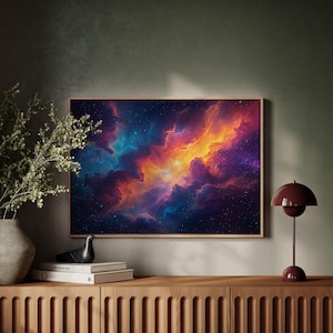 Puede incluir: Una obra de arte enmarcada que representa una nebulosa vibrante con nubes arremolinadas de color naranja, amarillo, azul y morado. La obra se exhibe sobre un mueble de madera, con un jarrón de vegetación y una lámpara de mesa burdeos.
