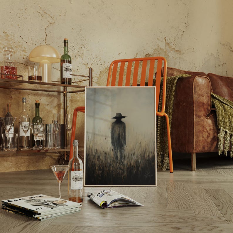 Peut inclure: Une &oelig;uvre encadr&eacute;e repr&eacute;sente une silhouette chapeaut&eacute;e dans les hautes herbes, avec une palette de couleurs sourdes. La sc&egrave;ne se d&eacute;roule dans une pi&egrave;ce avec un chariot de bar, une chaise orange et un canap&eacute; en cuir. Une bouteille de vin et un verre &agrave; cocktail sont au premier plan.
