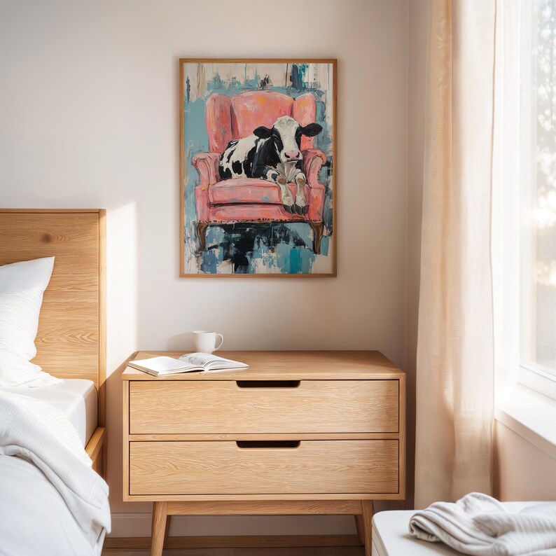 Puede incluir: Una pintura enmarcada de una vaca negra y blanca sentada en un sill&oacute;n rosa. La pintura tiene un fondo azul y blanco.